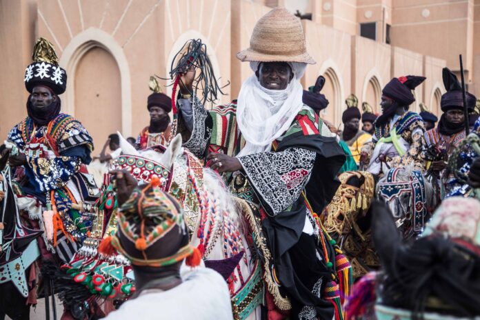 Uczestnicy barwnego festiwalu w Nigerii jadący na bogato zdobionych koniach Uczestnicy barwnego festiwalu w Nigerii jadący na bogato zdobionych koniach