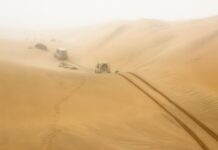 Dwa auta terenowe jadą przez rozległe wydmy w Namibii, region Hardap